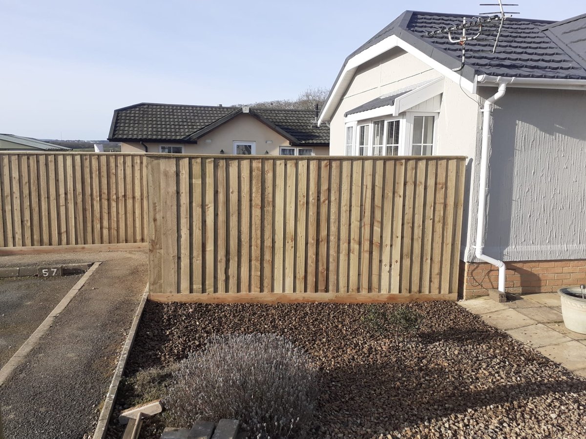 Backyard with wooden fence, gravel ground, and white suburban houses in background under clear sky