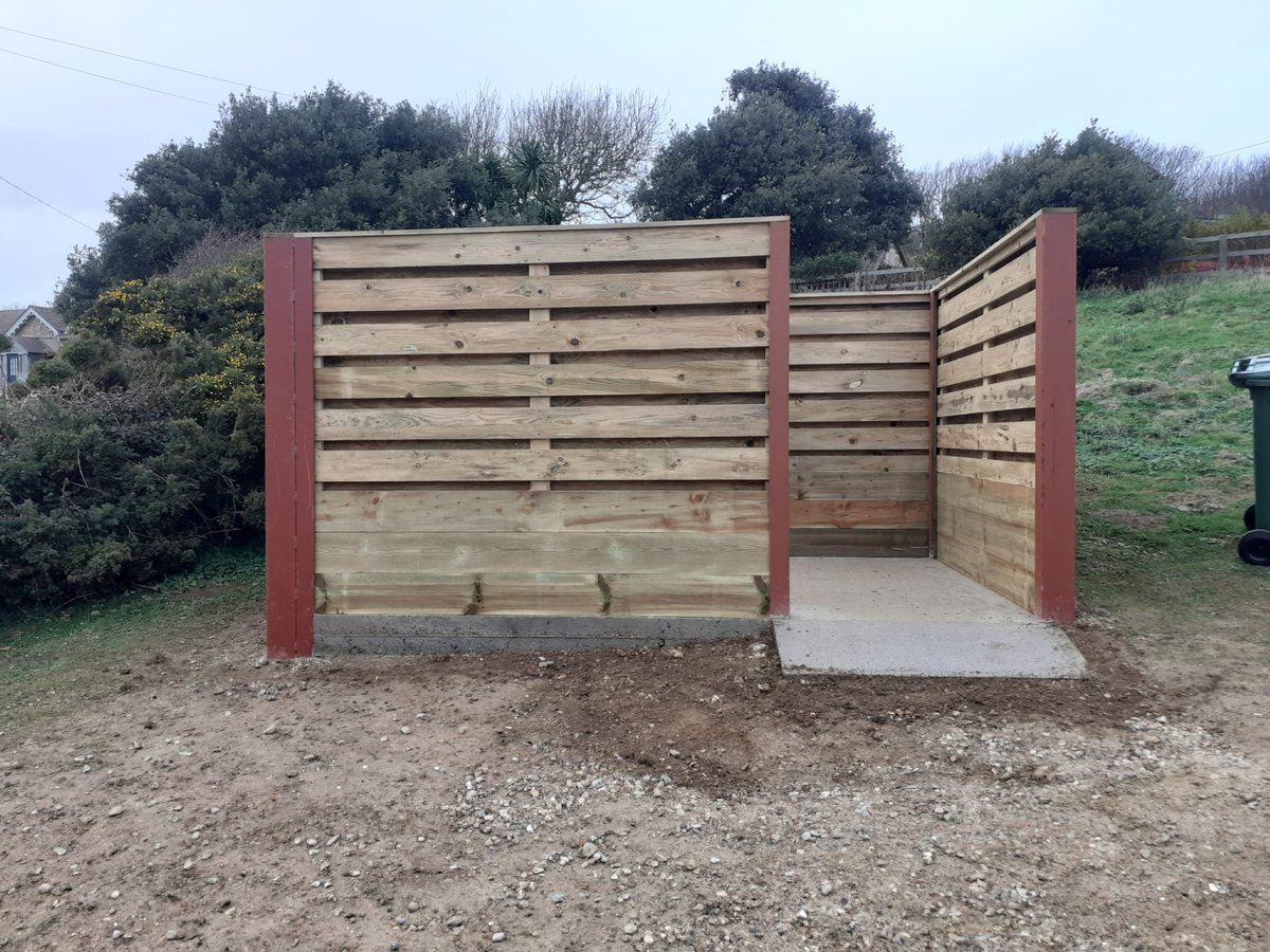 Three-sided wooden livestock shelter with red metal frame and open concrete floor in a rural field